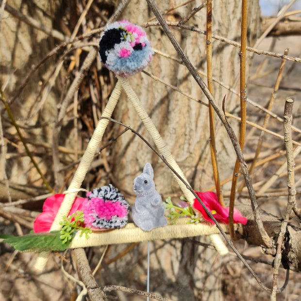 Lieldienu dekors - iekarināms trijstūris ar rozā ziediem / rozīgi pelēkiem dzijas bumbuļiem un pelēku kustināmu zaķi