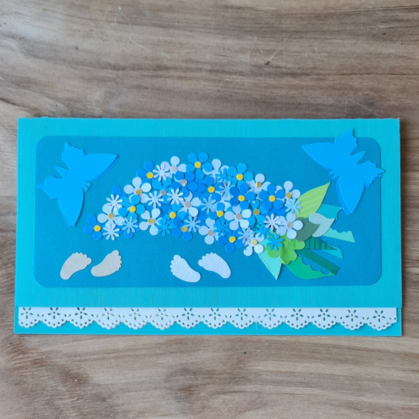 3D paper card for the birth or baptism of a boy. On a blue background, a bouquet of flowers, feet and butterflies with a lace-like edge 21 x 10.5 cm (AMA)