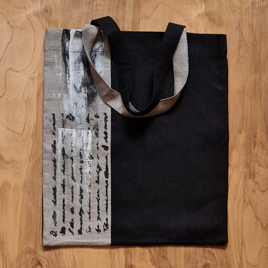 Nekrāsota un melna lina auduma iepirkumu maisiņš/soma ar vertikālu 2 joslu audumu maiņu / stilizētu melnu rokraksta dekorāciju uz lina krāsas auduma daļas un uz pleca liekamiem rokturiem (ZMI)