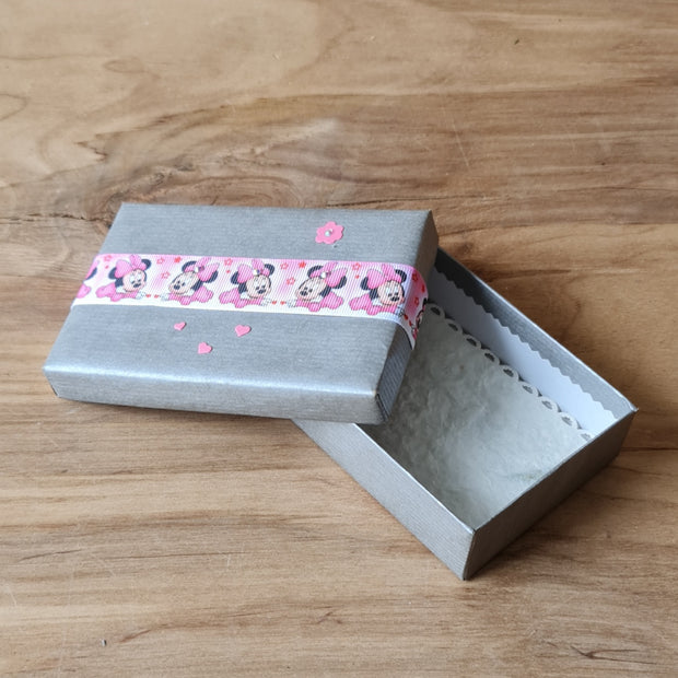 Dāvanu kārbiņa (iekšējie izmēri 11.8 x 7.8 cm) sudrabainā krāsā ar rozā mikipeles lentu uz vāka un gaišu iekšpusi (APU2)