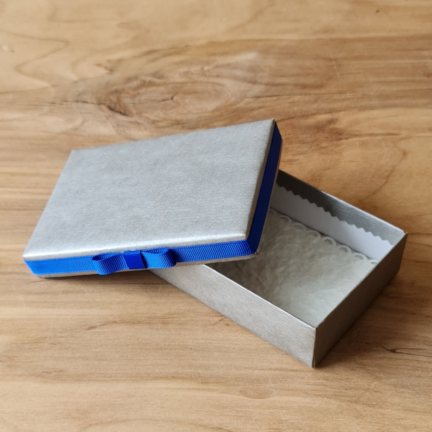 Gift box (inner dimensions 11.8 x 7.8 cm) in silver color with blue ribbon around the edge of the lid and light inside (APU2)