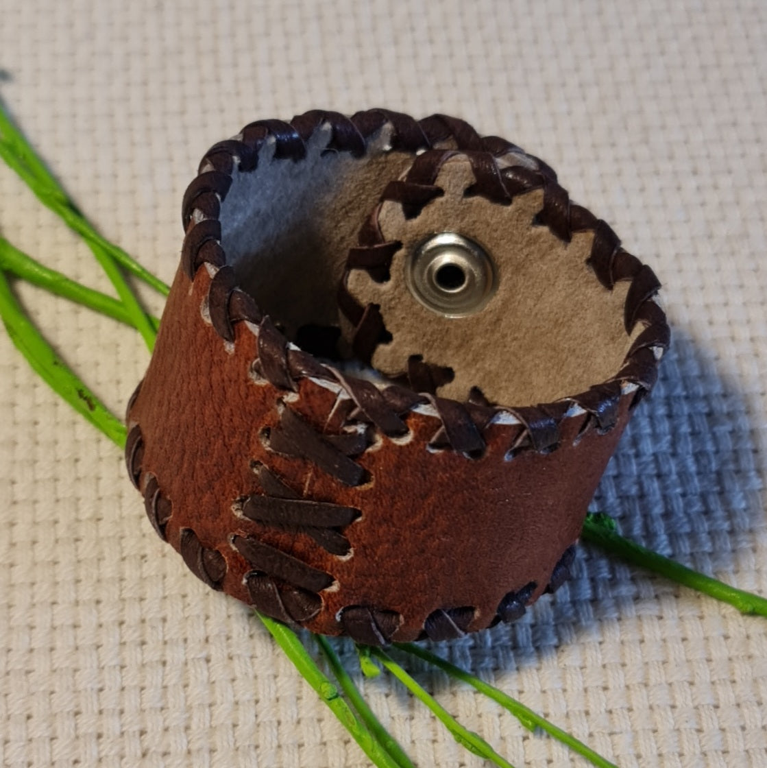 Band-shaped leather bracelet in brown color with dark brown cross-stitched decorative elements and push-button closure (JŠČ)