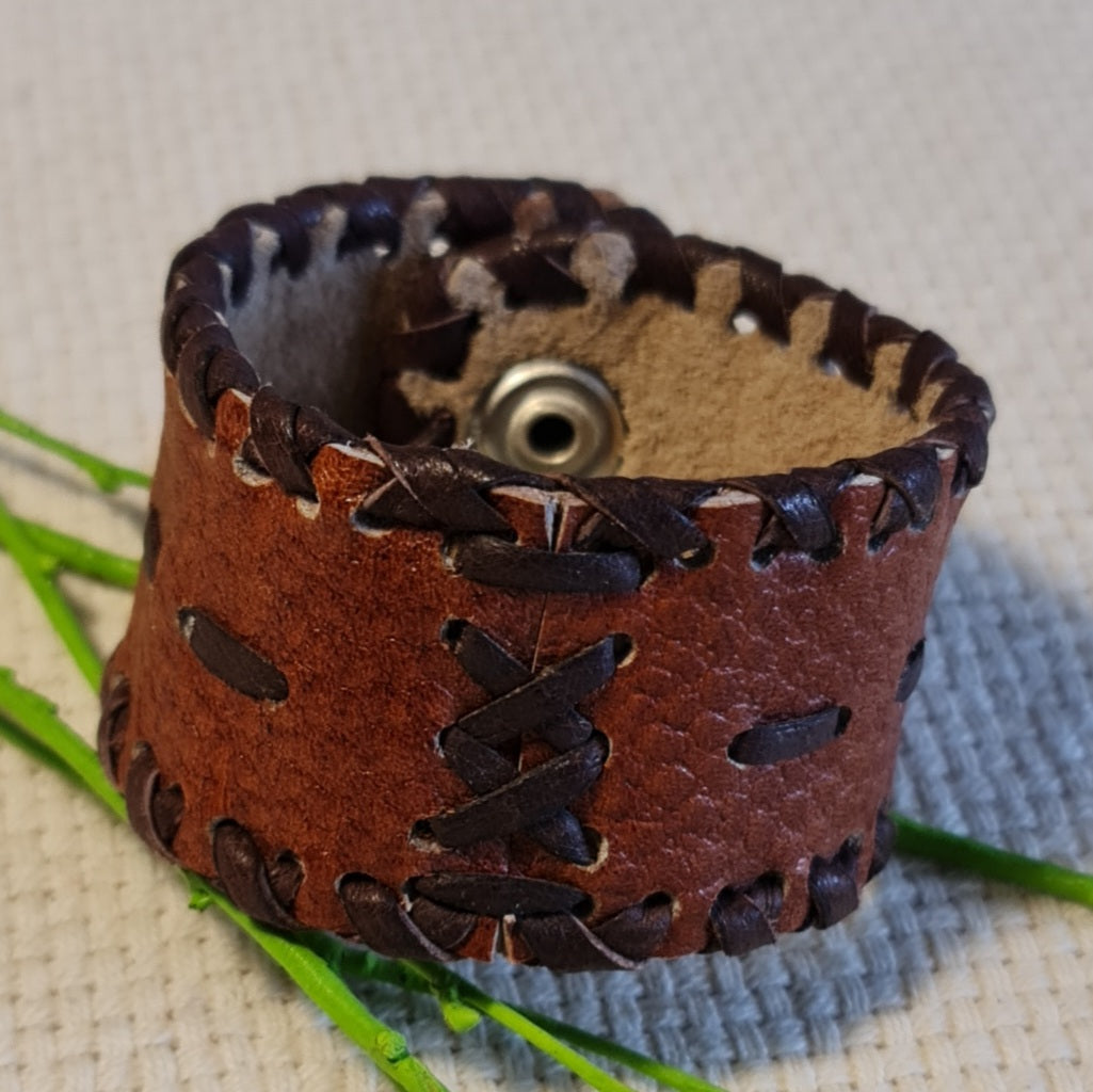 Band-shaped leather bracelet in brown color with dark brown cross and straight stitched decorative elements and push-button closure (JŠČ)