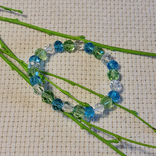 Gaiši zilu / gaiši zaļu / caurspīdīgu stikla pērlīšu rokassprādze vērta uz gumijas (diametrs 5.5 cm) (JŠČ)