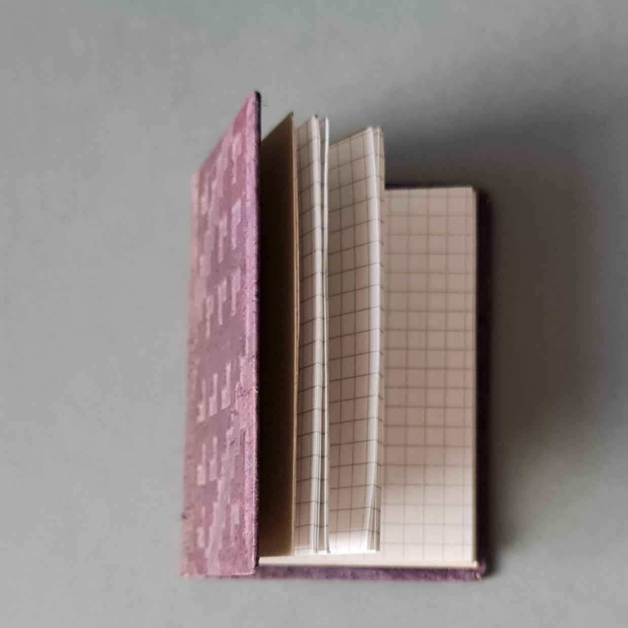 Rūtiņu bloknots ādas ievākojumā. Violetā krāsā ar dekoratīvu iespiedumu. 8 x 10.5 x 1 cm (MAPL 2) - www.tiptip.lv 